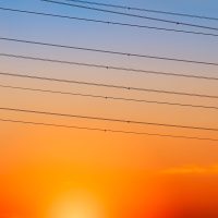 Silhouette high voltage electric pylon and electrical wire with an orange sky. Electricity poles at sunset. Power and energy concept. High voltage grid tower with wire cable at distribution station.